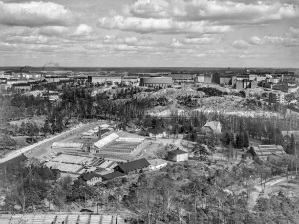 1938 - 1950 . Näkymä Stadionin tornista itään. Etualalla Kaupungin puutarhan tuotantoalue ja talvipuutarha, Hammarskjöldintie 1. Taustalla Alppila, Alppiharju ja Alppilan vesitorni nykyisen Linnanmäen alueella.